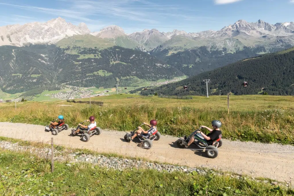 Ihr seht eine Gruppe junger Menschen, die mit den Mountaincarts Richtung Savognin ins Tal fahren