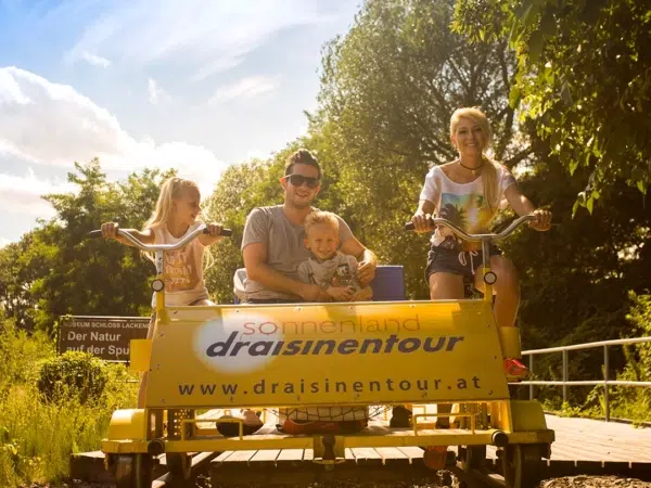 Ihr seht eine Familie bei einer Draisinentour durch das Sonnenland im Burgenland