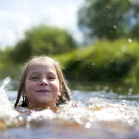 Sie sehen ein lachendes Kind beim Schwimmen in einem See in der Nähe von JUFA Hotels.