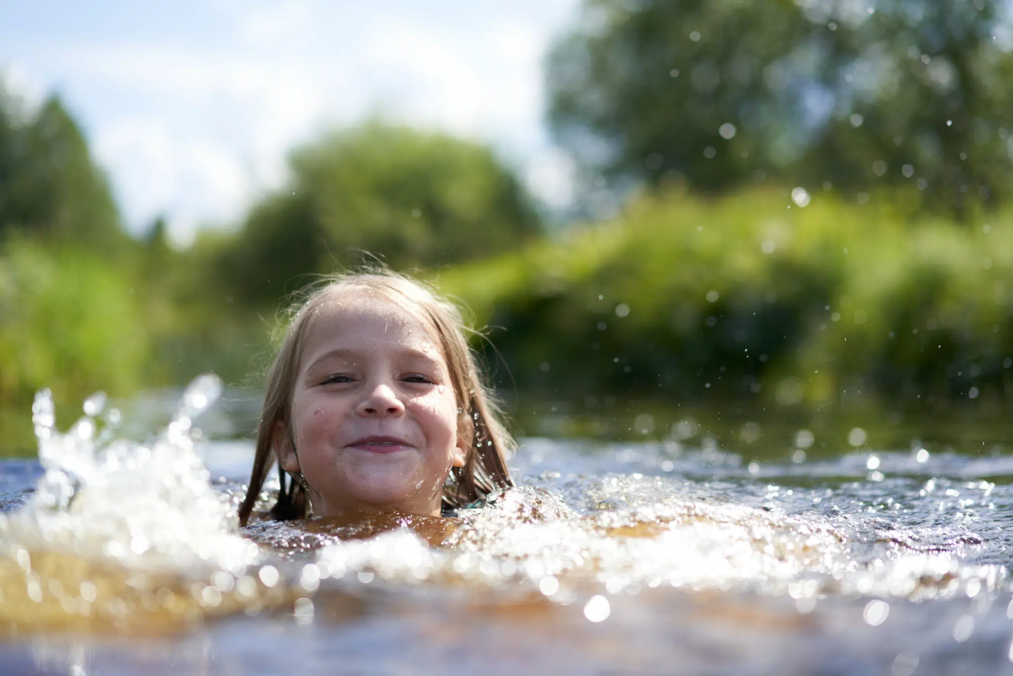 Sie sehen ein lachendes Kind beim Schwimmen in einem See in der Nähe von JUFA Hotels.