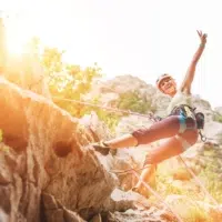 Smiling athletic woman in protective helmet and shoes climbing cliff rock wall using top rope and harness in Paklenica National park site in Croatia. Active extreme sports time spending concept