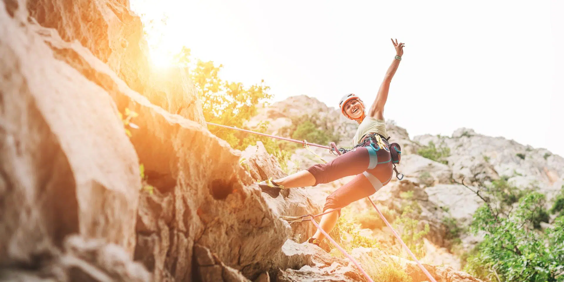 Smiling athletic woman in protective helmet and shoes climbing cliff rock wall using top rope and harness in Paklenica National park site in Croatia. Active extreme sports time spending concept