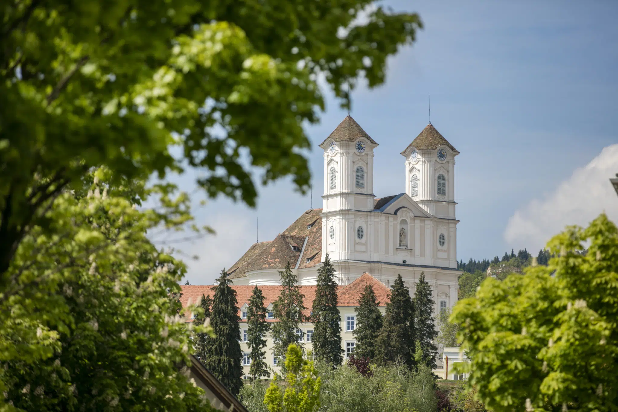 Ihr seht die Basilika am Weizberg mit ihren Stiftstürmen. JUFA Hotels bietet erholsamen Familienurlaub und einen unvergesslichen Winter- und Wanderurlaub.