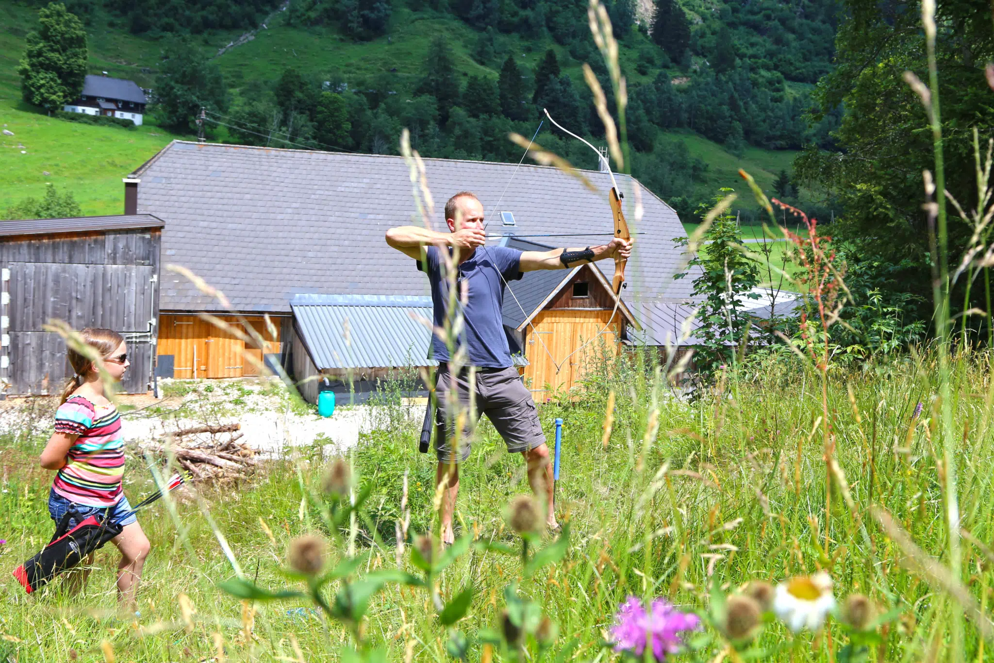 Sie sehen einen Mann und ein Mädchen beim Bogenschießen auf dem Schaupphof in Donnersbach. JUFA Hotels bietet kinderfreundlichen und erlebnisreichen Urlaub für die ganze Familie.