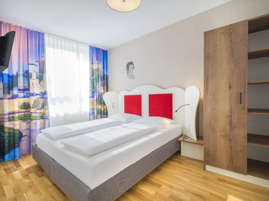 Ihr seht ein Doppelbett in einer Suite4 mit Couch im JUFA Hotel Salzburg City.