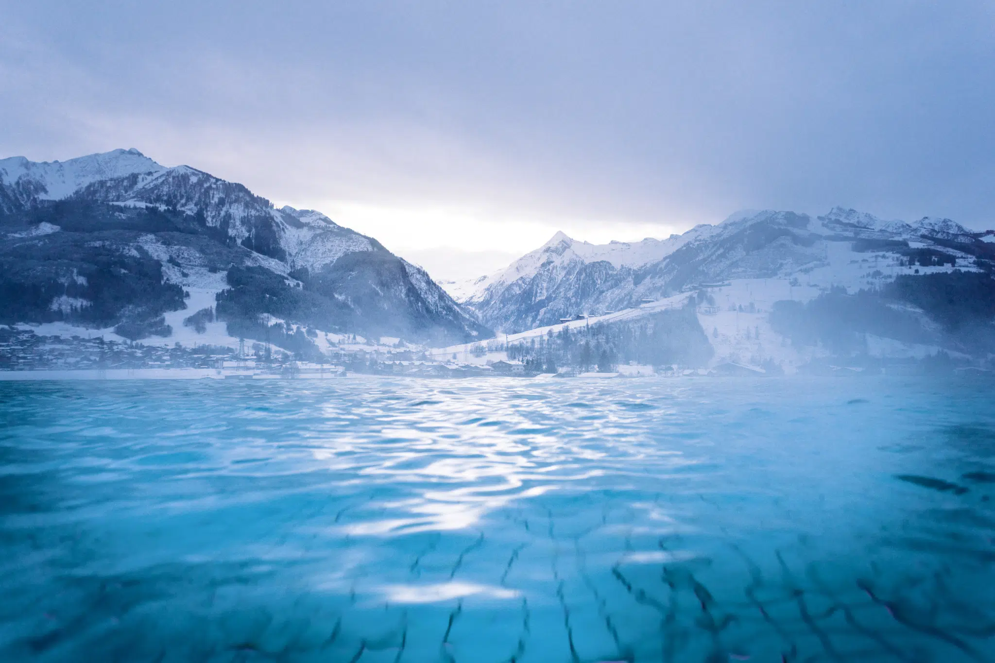 Ihr seht den Outdoor-Pool vom Tauern SPA Kaprun im Winter mit Blick auf die verschneite Bergwelt.