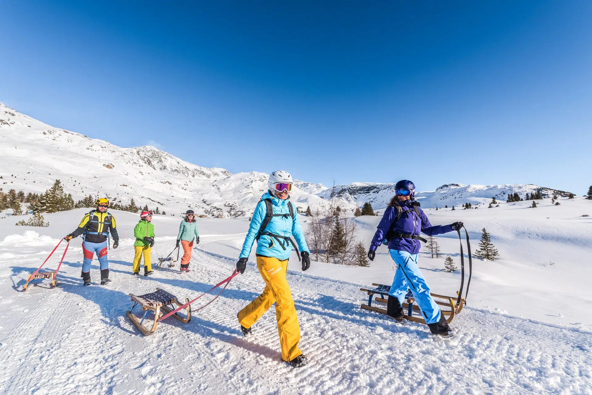 Ihr seht eine Familie mit Rodeln in Savognin. JUFA Hotels bietet erholsamen Familienurlaub und einen unvergesslichen Winterurlaub.