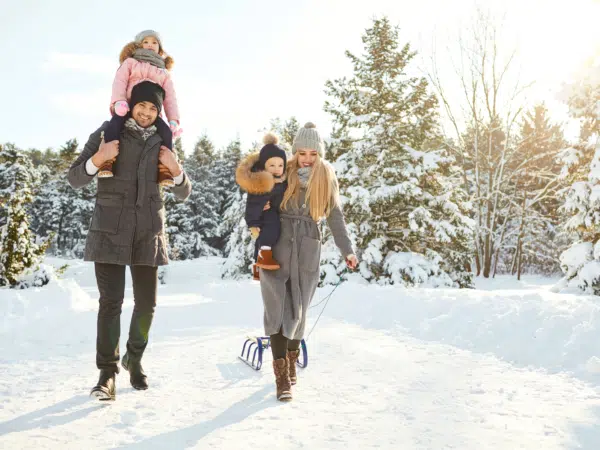 Ihr seht eine Familie. die glücklich mit einem Schlitten über den schneebedckten Weg läuft. JUFA Hotels bietet kinderfreundlichen und erlebnisreichen Urlaub für die ganze Familie.