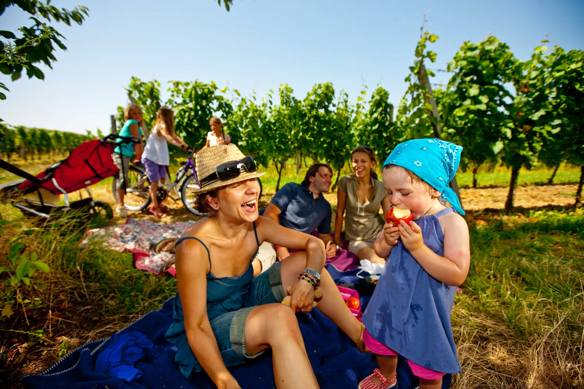 Familie hat Spass beim Picknick in der Natur und Kind beisst in Apfel im Burgenland. JUFA Hotels bietet erholsamen Familienurlaub und einen unvergesslichen Winter- und Wanderurlaub.