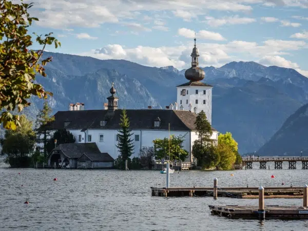 Ihr seht das Seeschloss Ort im Traunsee vor einer Bergkulisse.