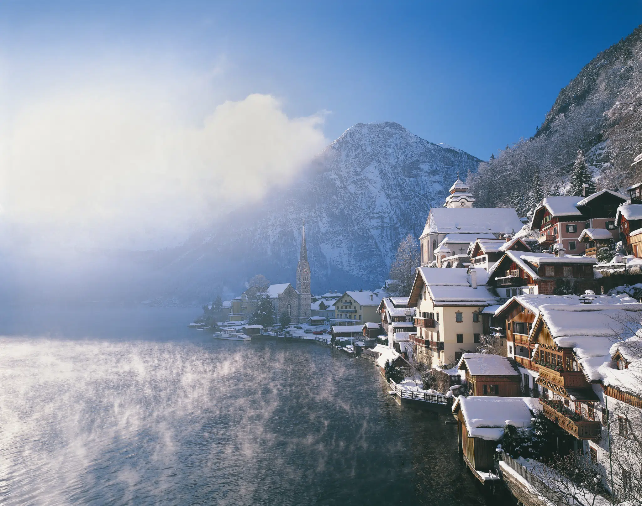 Ihr seht Hallstatt im Salzkammergut mit schneebedeckten Hausdächern im Winter in der Nähe von JUFA Hotels. Der Ort für erholsamen Familienurlaub und einen unvergesslichen Winter- und Wanderurlaub.