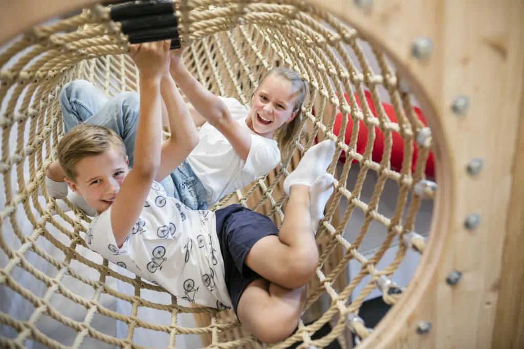 Ihr seht Kinder im Kletternetz im JUFA Hotel Weiz. Der Ort für kinderfreundlichen und erlebnisreichen Urlaub für die ganze Familie.