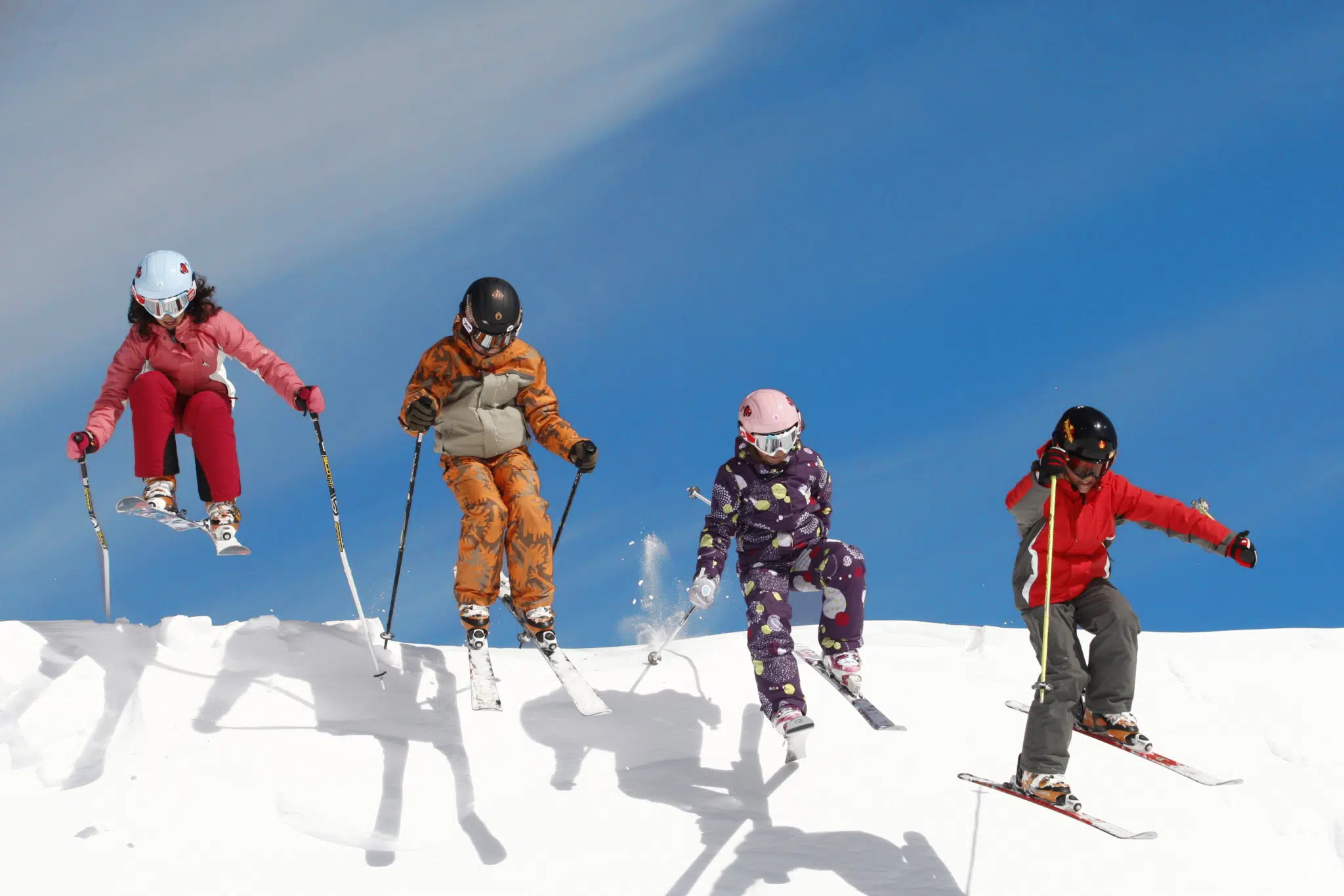 Ihr seht vier Kinder beim Springen beim Skifahren im Winter.