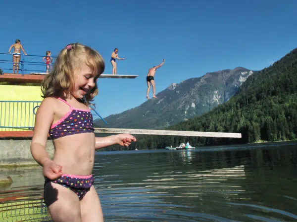 Ihr seht ein Mädchen am Seebad am Lunzer See mit Sprungturm und Menschen im Hintergrund. JUFA Hotels bietet kinderfreundlichen und erlebnisreichen Urlaub für die ganze Familie.