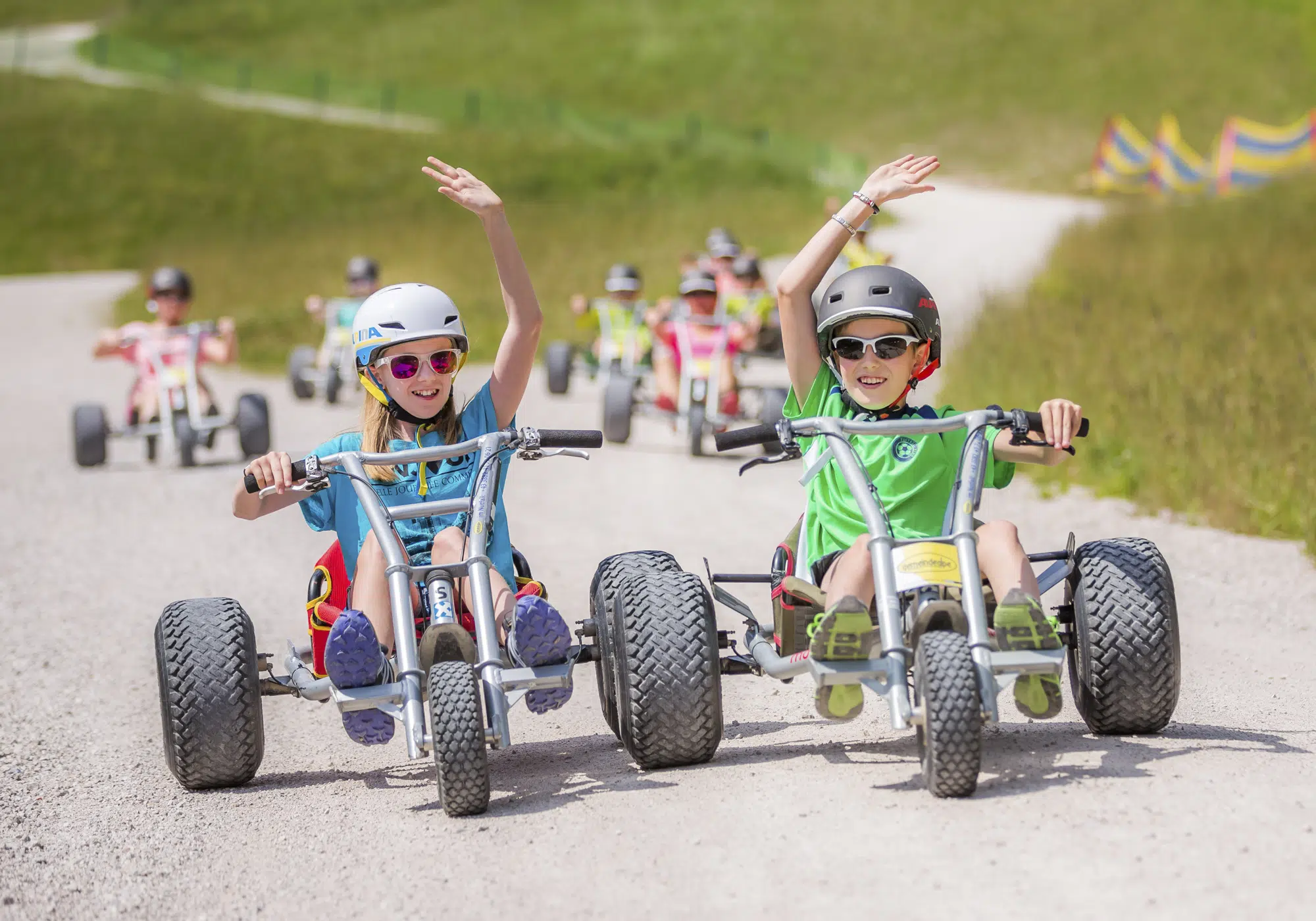 Ihr seht Kinder auf Mountaincarts auf einem Kiesweg auf der Mariazeller Gemeindealpe in der Nähe von JUFA Hotels fahren. Der Ort für erholsamen Familienurlaub und einen unvergesslichen Winter- und Wanderurlaub.