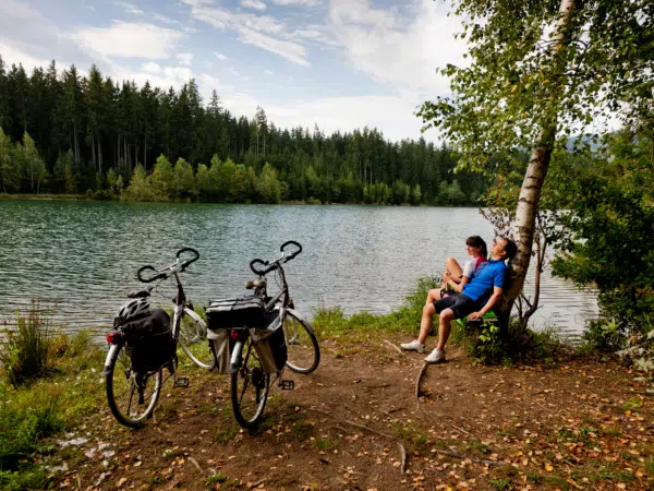 Ihr seht den Murradweg im Murtal mit der Mur und einem rastenden Paar im Sommer. JUFA Hotels bietet erholsamen Familienurlaub und einen unvergesslichen Winter- und Wanderurlaub.