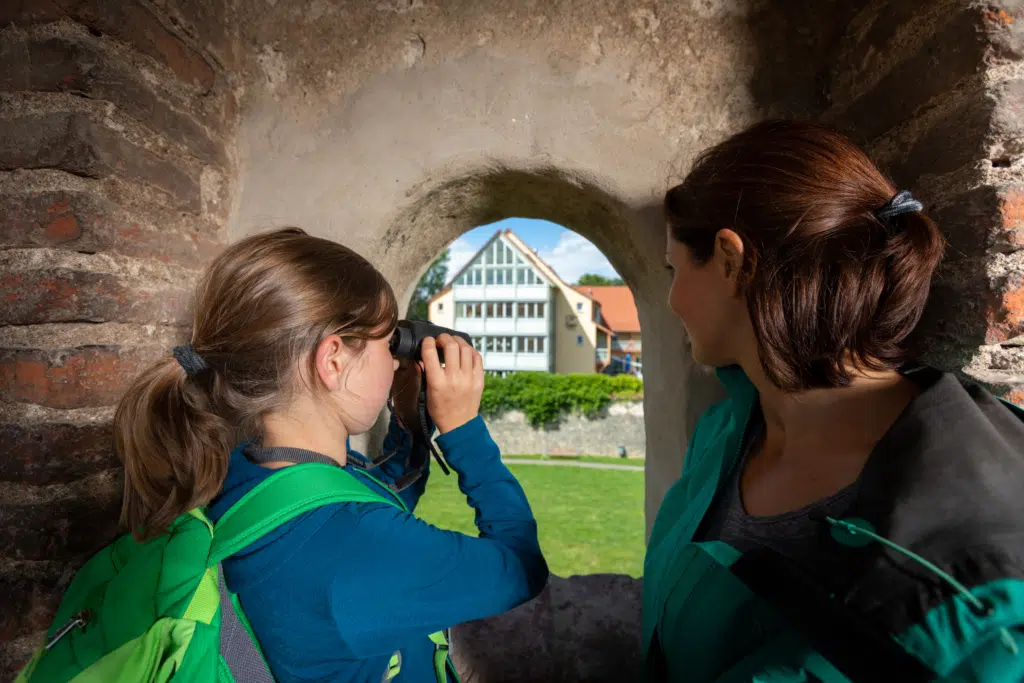 Ihr seht ein Mädchen beim Fotografieren des JUFA Hotels Nördlingen, durch die historische Stadtmauer. JUFA Hotels, der Ort für kinderfreundlichen und erlebnisreichen Urlaub für die ganze Familie.