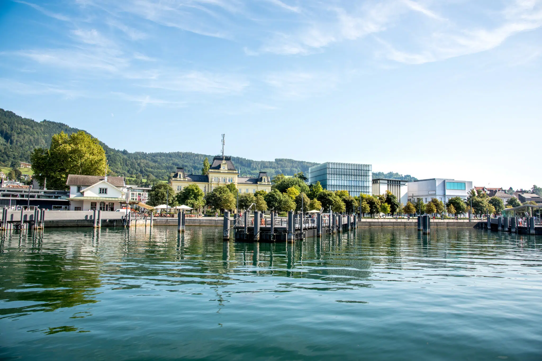 Ihr seht ein Panorama von Bregenz im Sommer vom Hafen aus mit der Post und dem Kunsthaus.