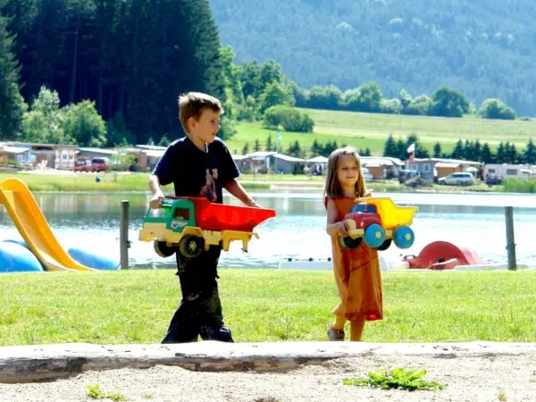 Zwei Kinder mit Sandspielzeug am Badestrand vom Pirkdorfer See in der Nähe vom JUFA Hotel Bleiburg/Pliberk***.