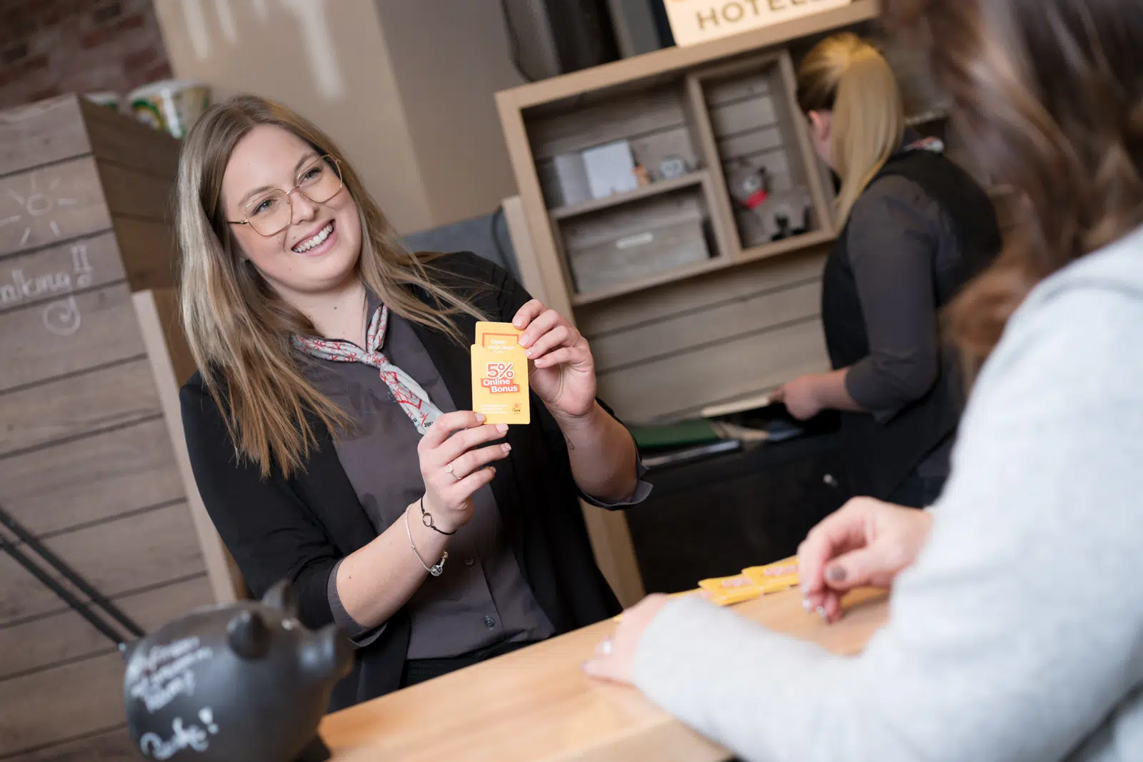 Ihr seht eine Rezeptionistin mit einer Zimmerkarte in der Hand für einen Gast. JUFA Hotels sind das ganze Jahr der ideale Ort für einen abwechslungsreichen Urlaub für die ganze Familie.