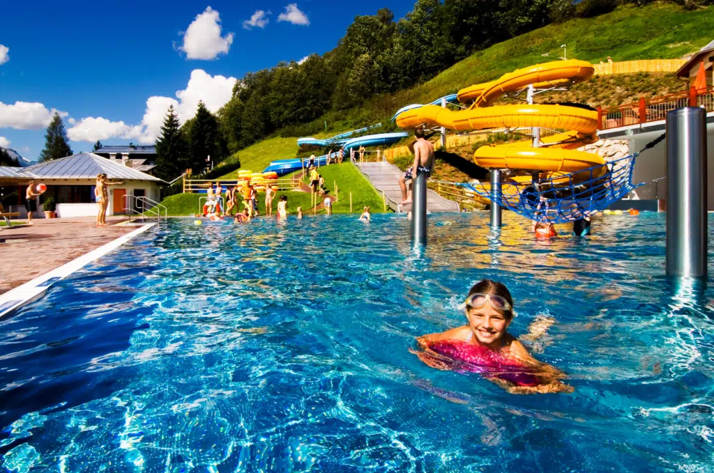 Sie sehen das Freibad Saalbach mit Rutsche im Sommer in der Nähe vom JUFA Alpenhotel Saalbach****. Der Ort für kinderfreundlichen und erlebnisreichen Urlaub für die ganze Familie.