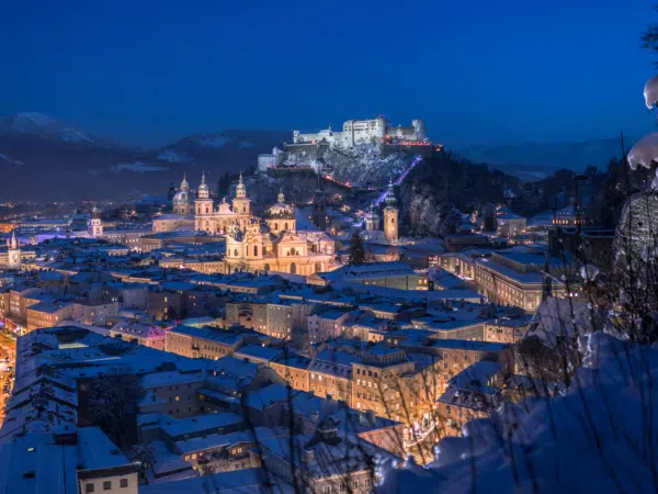 Ihr seht den Blick vom Mönchsberg auf die winterliche Festung Hohensalzburg mit Abendstimmung.