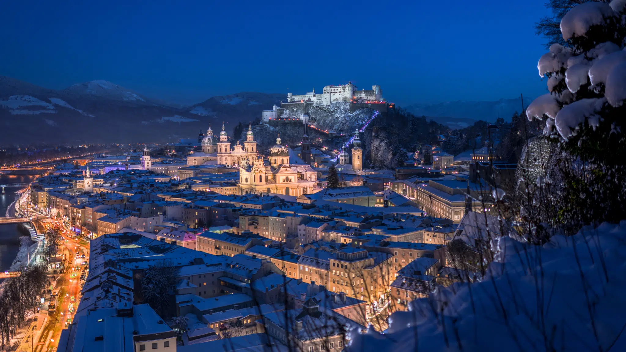 Ihr seht den Blick vom Mönchsberg auf die winterliche Festung Hohensalzburg mit Abendstimmung.