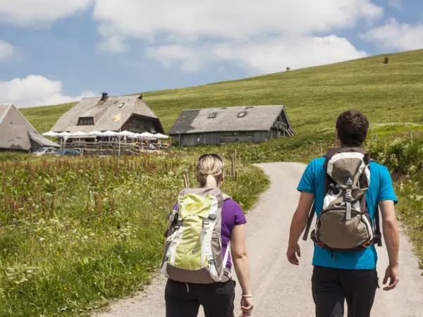 Ihr seht ein Paar, das auf einer Wanderung am Feldberg bei der nächsten Hütte einkehrt. JUFA Hotels bietet Ihnen den Ort für erlebnisreichen Natururlaub für die ganze Familie.