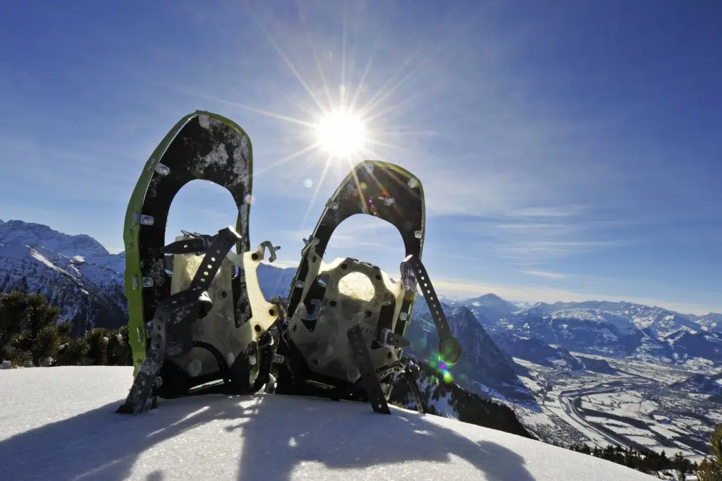 Ein paar Schneeschuhe steckt vor einem winterlichen Bergpanorama im Schnee. JUFA Hotels bietet erholsamen Familienurlaub und einen unvergesslichen Winterurlaub.