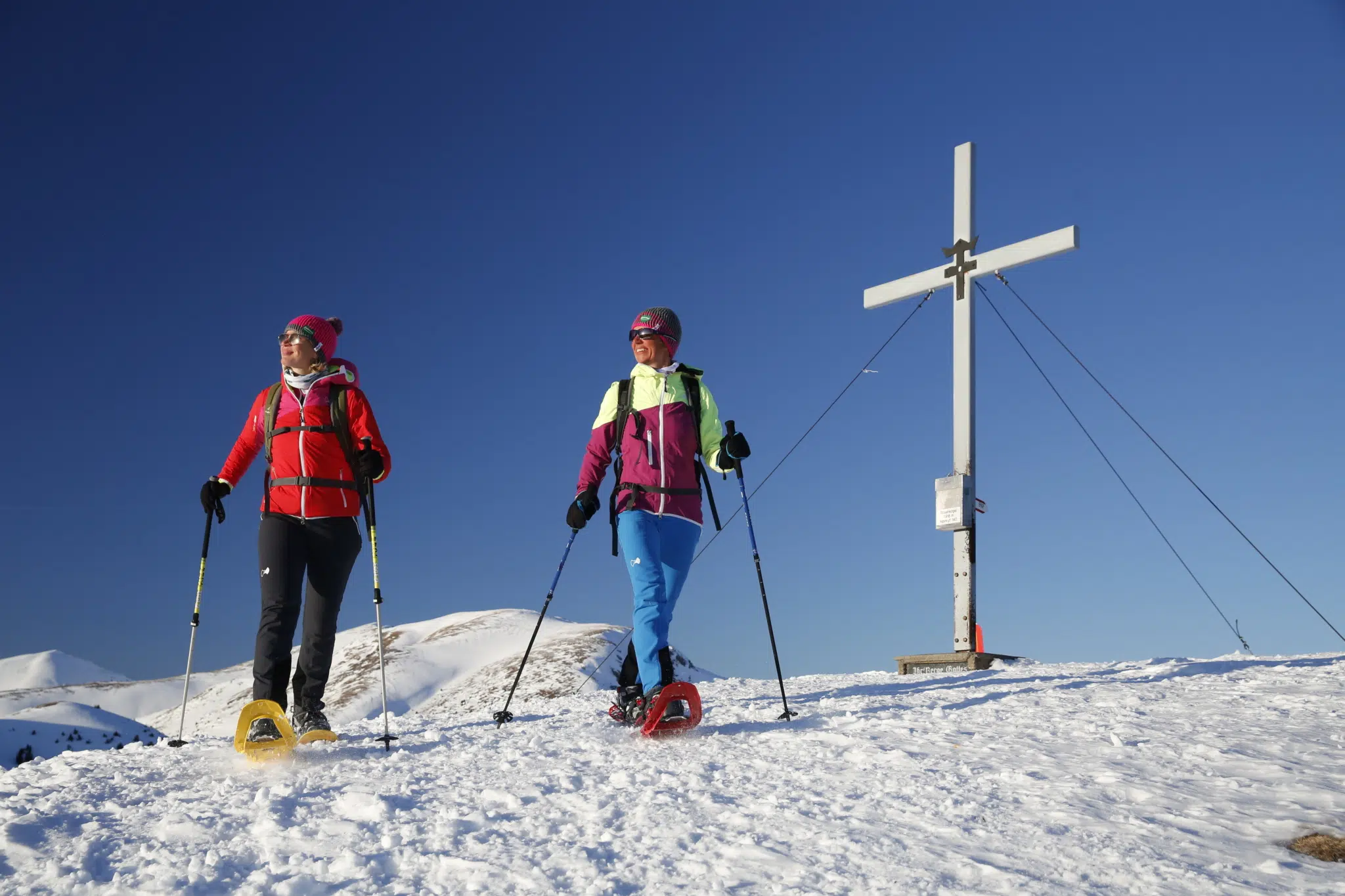 Ihr seht Schneeschuhwanderer an einem Gipfelkreuz im Murtal im Winter. JUFA Hotels bietet erholsamen Familienurlaub und einen unvergesslichen Winterurlaub.