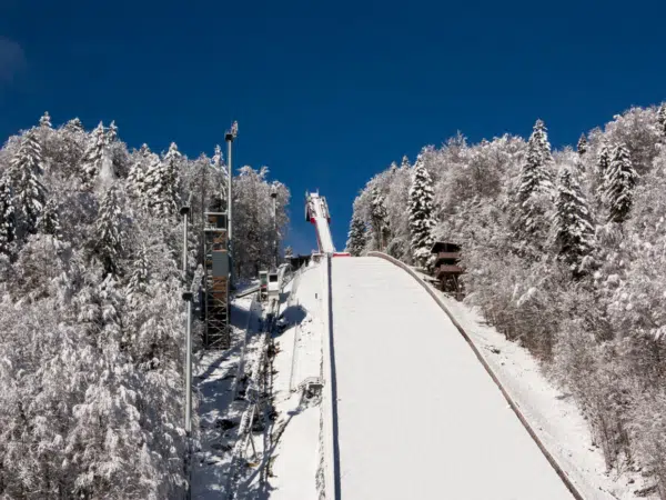 Ihr seht die Skiflugschanze in Oberstdorf umgeben von verschneiter Landschaft und Bäumen.