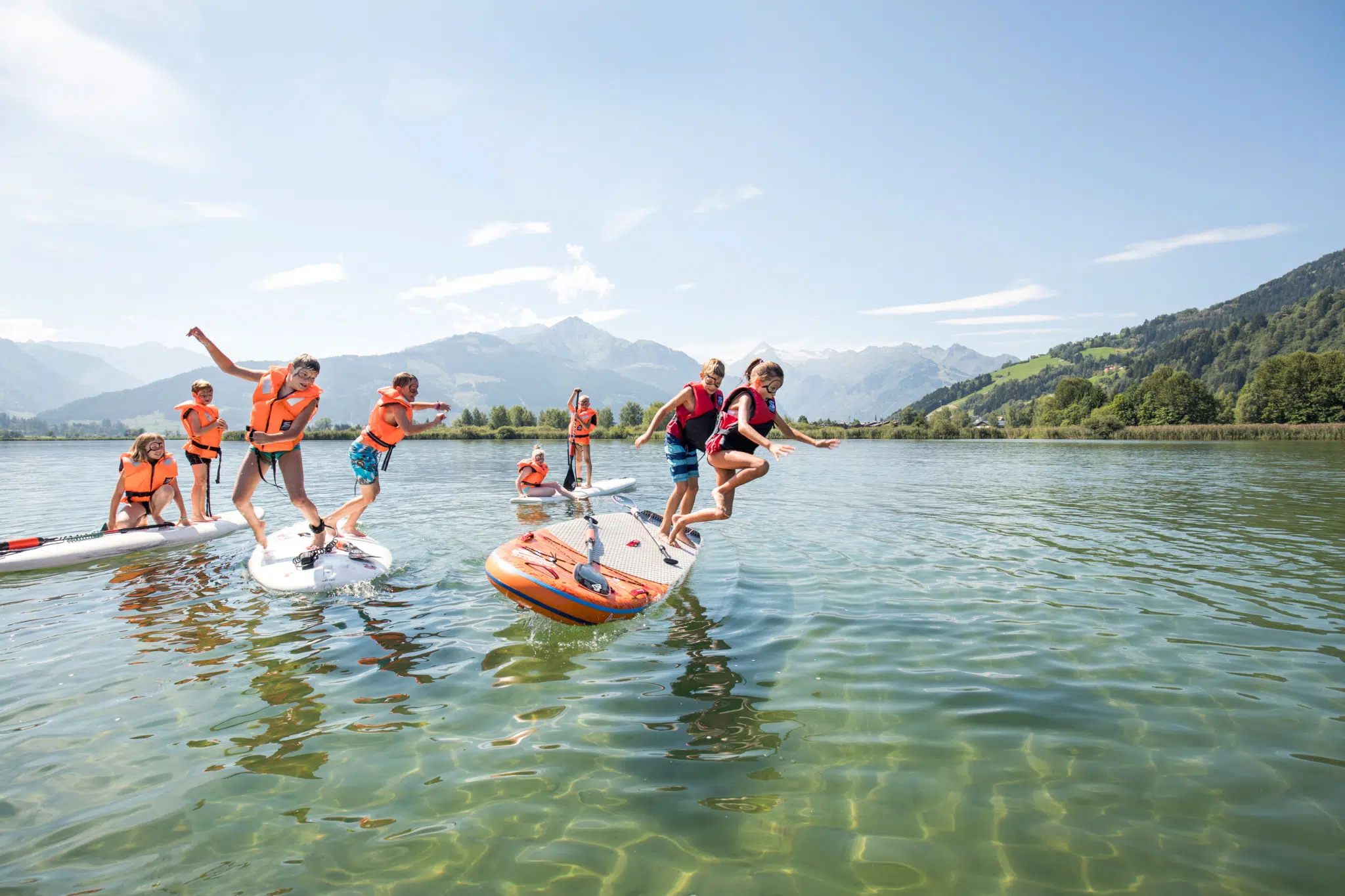 Sie sehen Kinder im Zeller See, die von einem SUP ins Wasser springen. JUFA Hotels bietet erholsamen Familienurlaub und einen unvergesslichen Wanderurlaub.