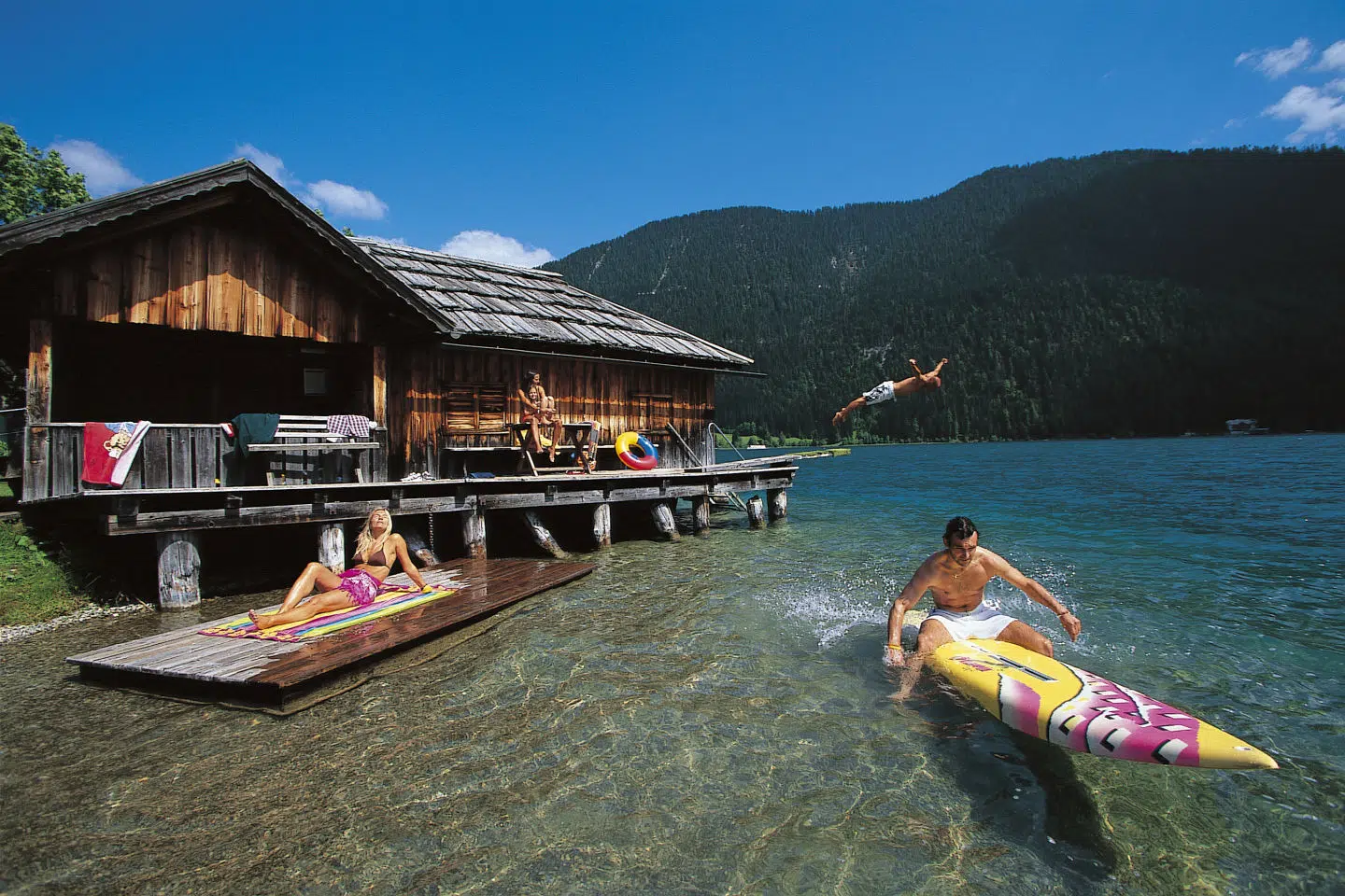 Ihr seht eine Familie, die sich am Weissensee in Kärnten mit Surfbrettern im Sommer vergnügt.