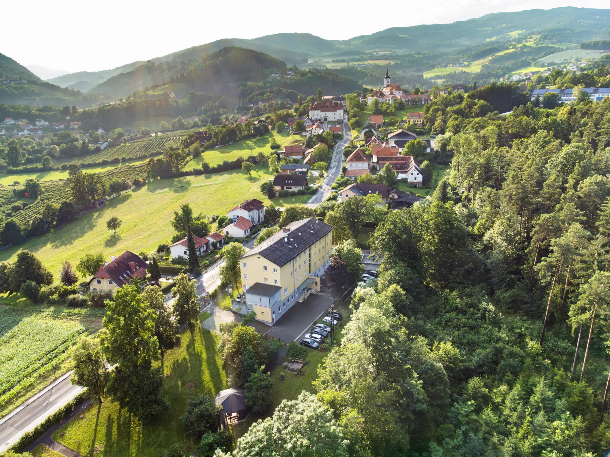 Ihr seht ein Panoramabild aus der Vogelperspektive vom JUFA Hotel Garni Stubenberg mit dem Ortszentrum von Stubenberg sowie den umliegenden Wiesen und Wäldern.