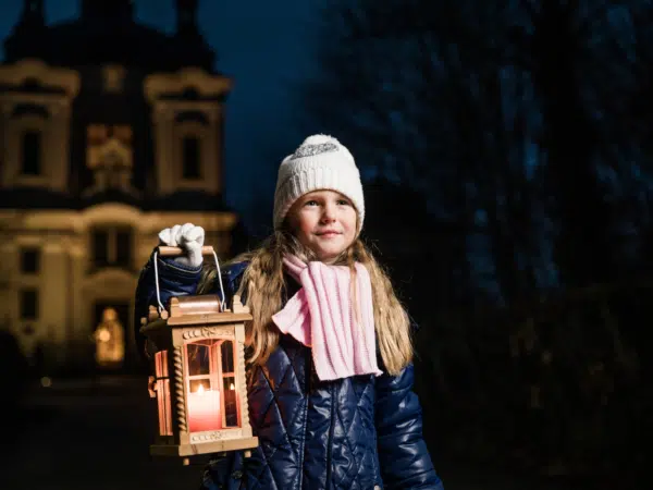 Ihr seht ein kleines Mädchen mit einer Laterne in der Hand beim Advent in Oberösterreich im Winter.