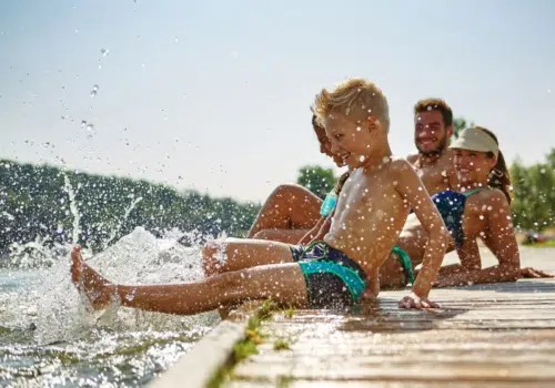 Ihr seht eine Familie beim Baden am Steg. JUFA Hotels bietet tollen Sommerurlaub an schönen Seen für die ganze Familie.