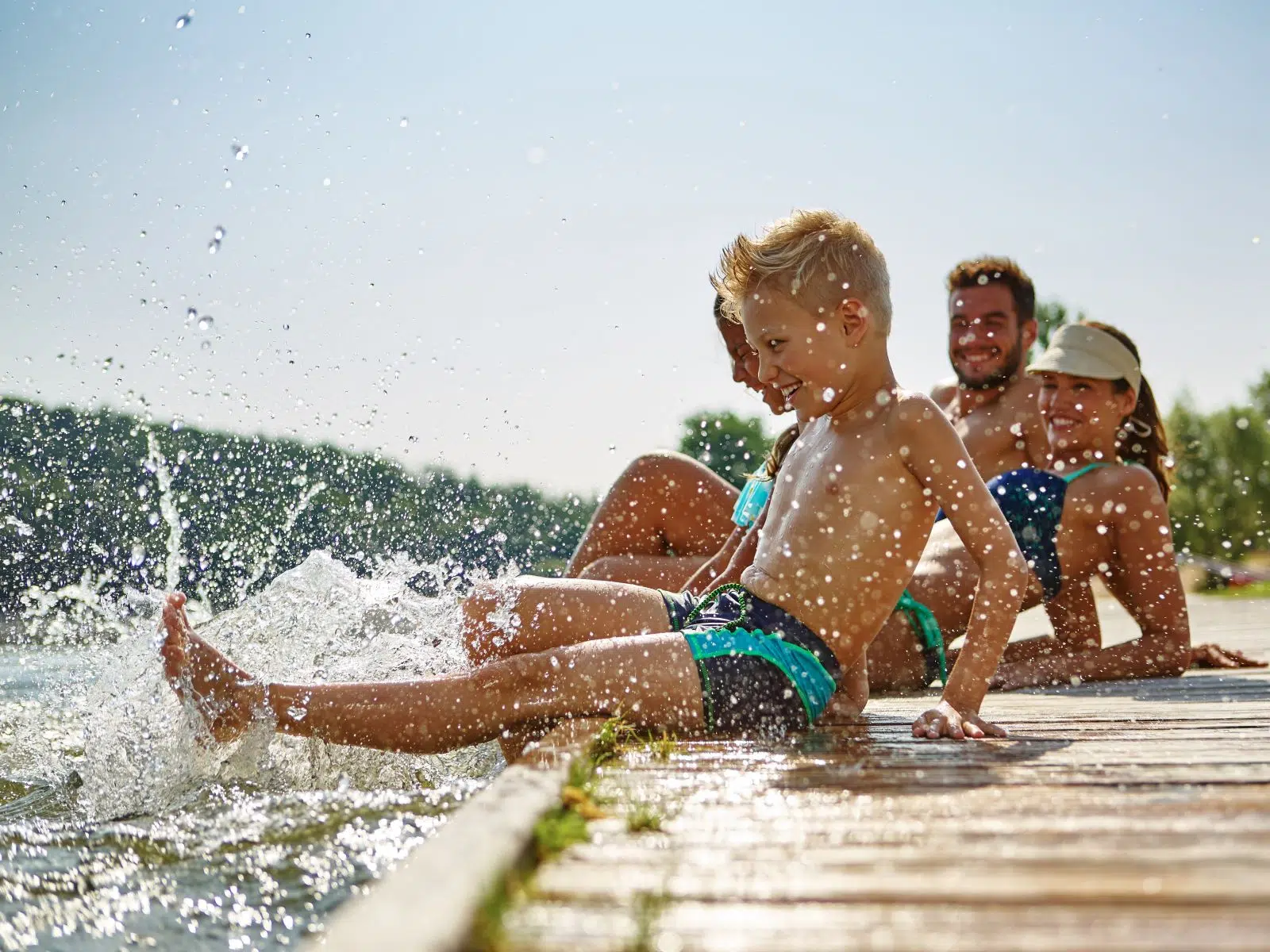 Ihr seht eine Familie beim Baden am Steg. JUFA Hotels bietet tollen Sommerurlaub an schönen Seen für die ganze Familie.