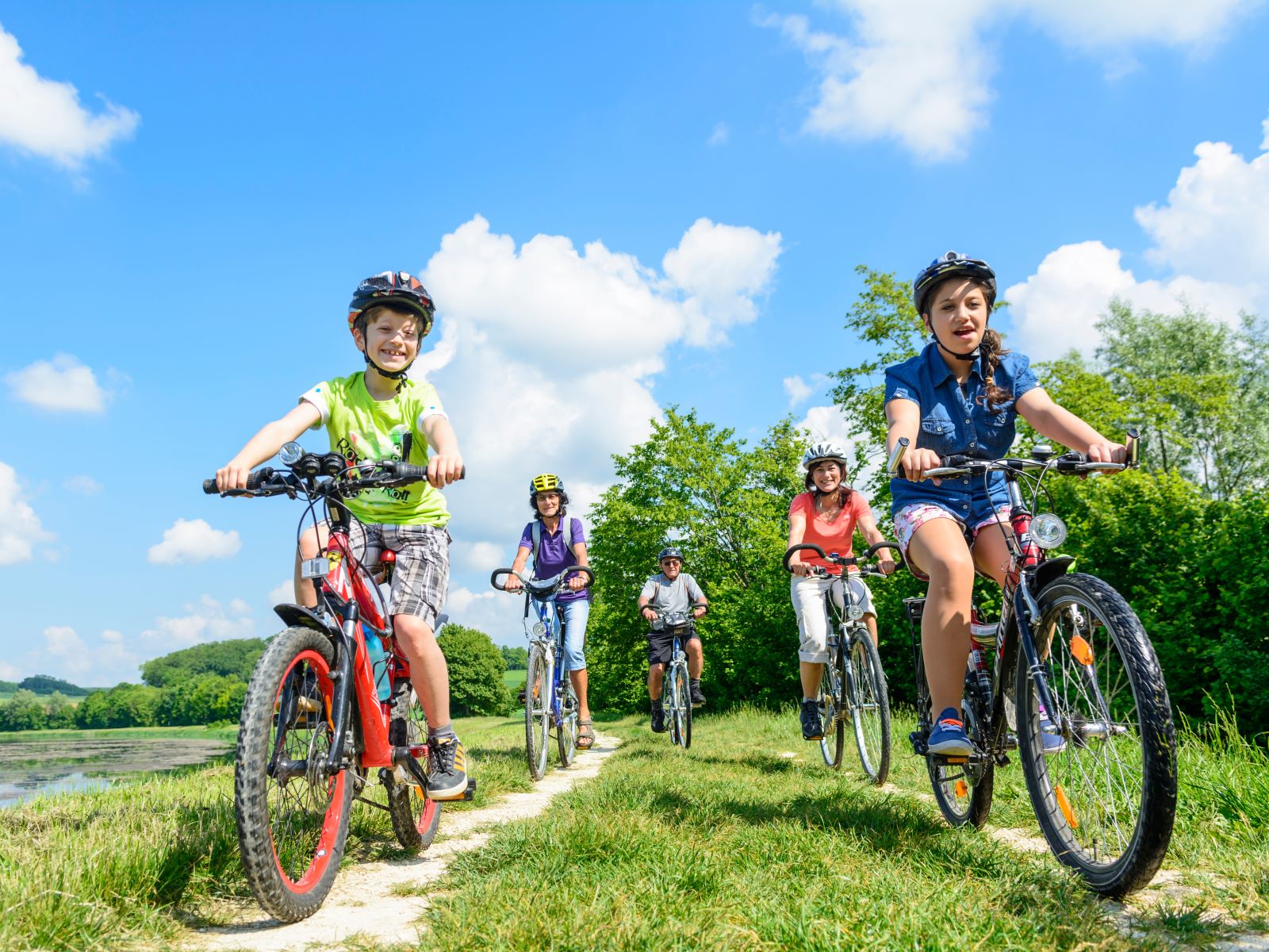 Ihr seht eine Familie, die neben einem Teich mit ihren Fahrrädern fahren. JUFA Hotels bietet kinderfreundlichen und erlebnisreichen Urlaub für die ganze Familie.