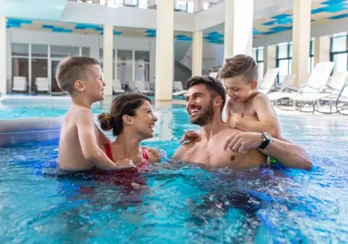 Ihr seht eine Familie mit Kindern beim Baden und Entspannen im Innenbereich einer Therme in der Nähe von JUFA Hotels.