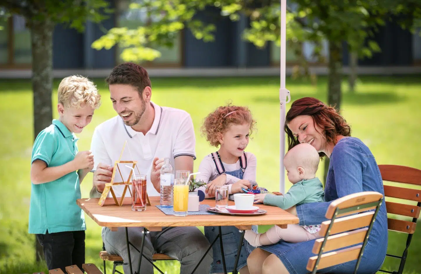 Ihr seht den Garten des JUFA Hotels Mariazell-Erlaufsee mit Familie beim Spielen und Getränken.