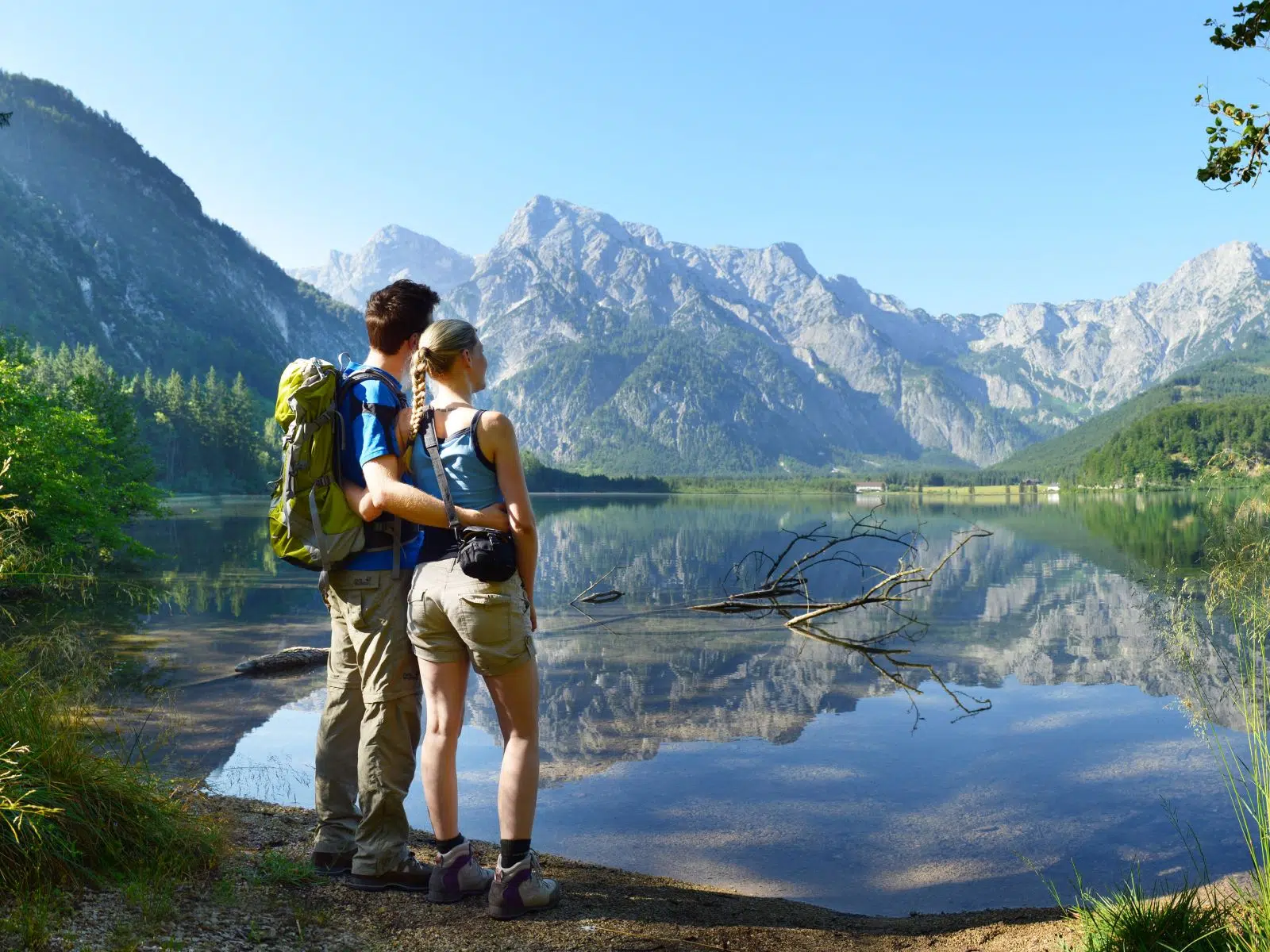 Ihr seht zwei Wanderer vor dem Bergpanorama des Almsees im Sommer.