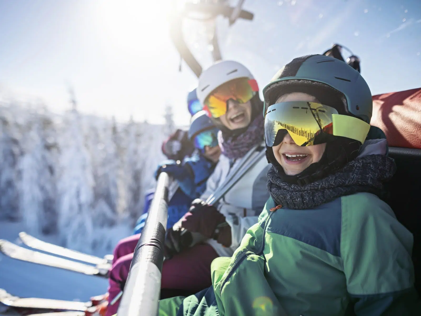 Ihr seht Kinder und Erwachsene beim Skifahren in den Alpen auf dem Sessellift.