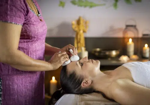 Ihr seht eine Frau, die sich bei einer angenehmen Kräuterstempelmassage im Tulsi Ayurveda-Zentrum im JUFA Hotel Stift Gurk entspannt. Der Ort für kinderfreundlichen und erlebnisreichen Urlaub für die ganze Familie.