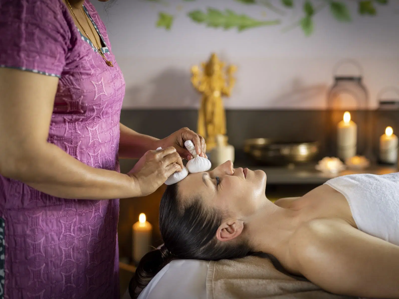 Ihr seht eine Frau, die sich bei einer angenehmen Kräuterstempelmassage im Tulsi Ayurveda-Zentrum im JUFA Hotel Stift Gurk entspannt. Der Ort für kinderfreundlichen und erlebnisreichen Urlaub für die ganze Familie.