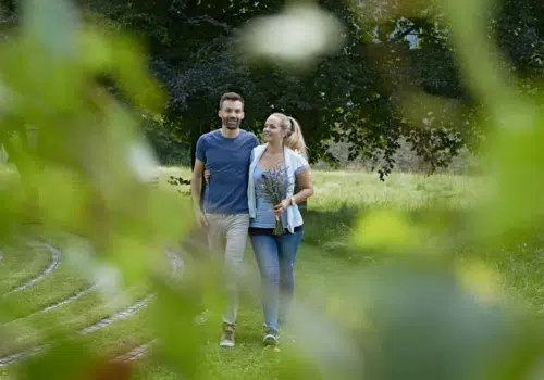 Ihr seht ein Paar im Garten beim Spaziergang im Sommer. JUFA Hotels bietet Ihnen den Ort für erlebnisreichen Natururlaub für die ganze Familie.