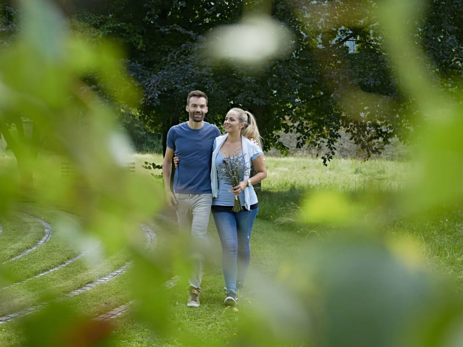 Ihr seht ein Paar im Garten beim Spaziergang im Sommer. JUFA Hotels bietet Ihnen den Ort für erlebnisreichen Natururlaub für die ganze Familie.