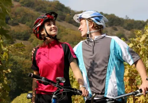 Ihr seht ein Paar, das in einem Weingarten eine Pause vom Radfahren macht.