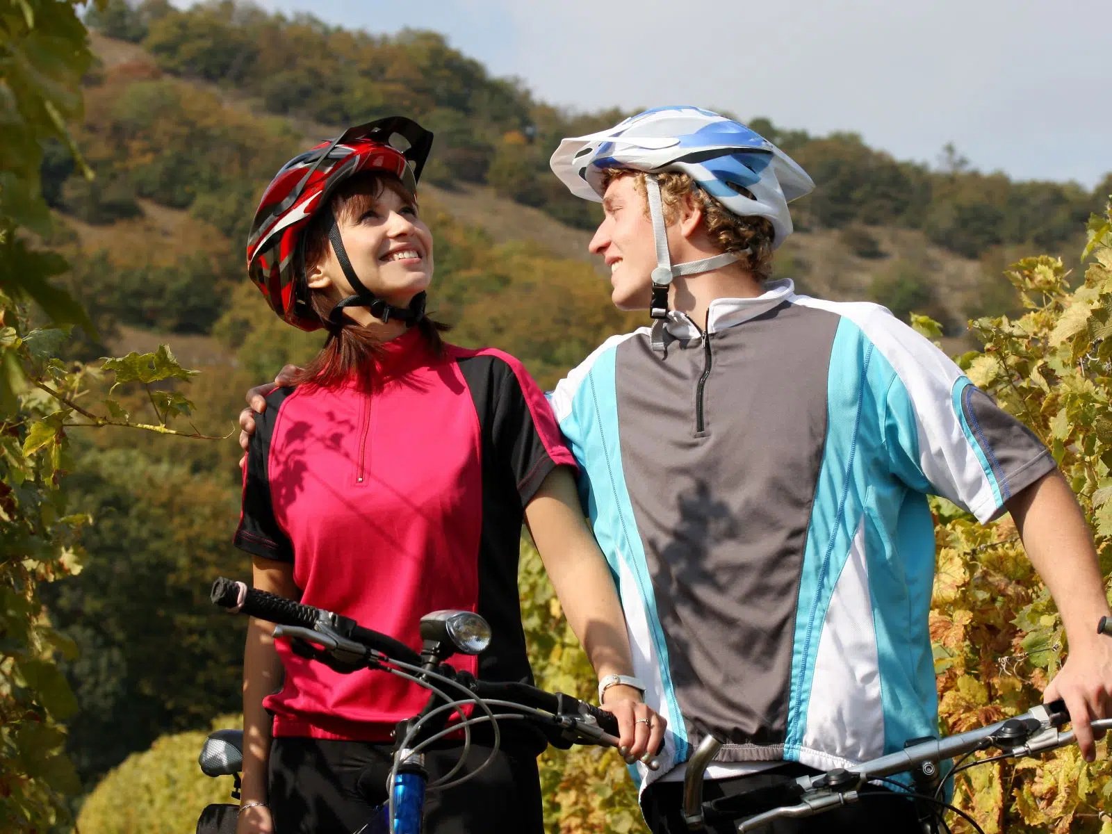 Ihr seht ein Paar, das in einem Weingarten eine Pause vom Radfahren macht.