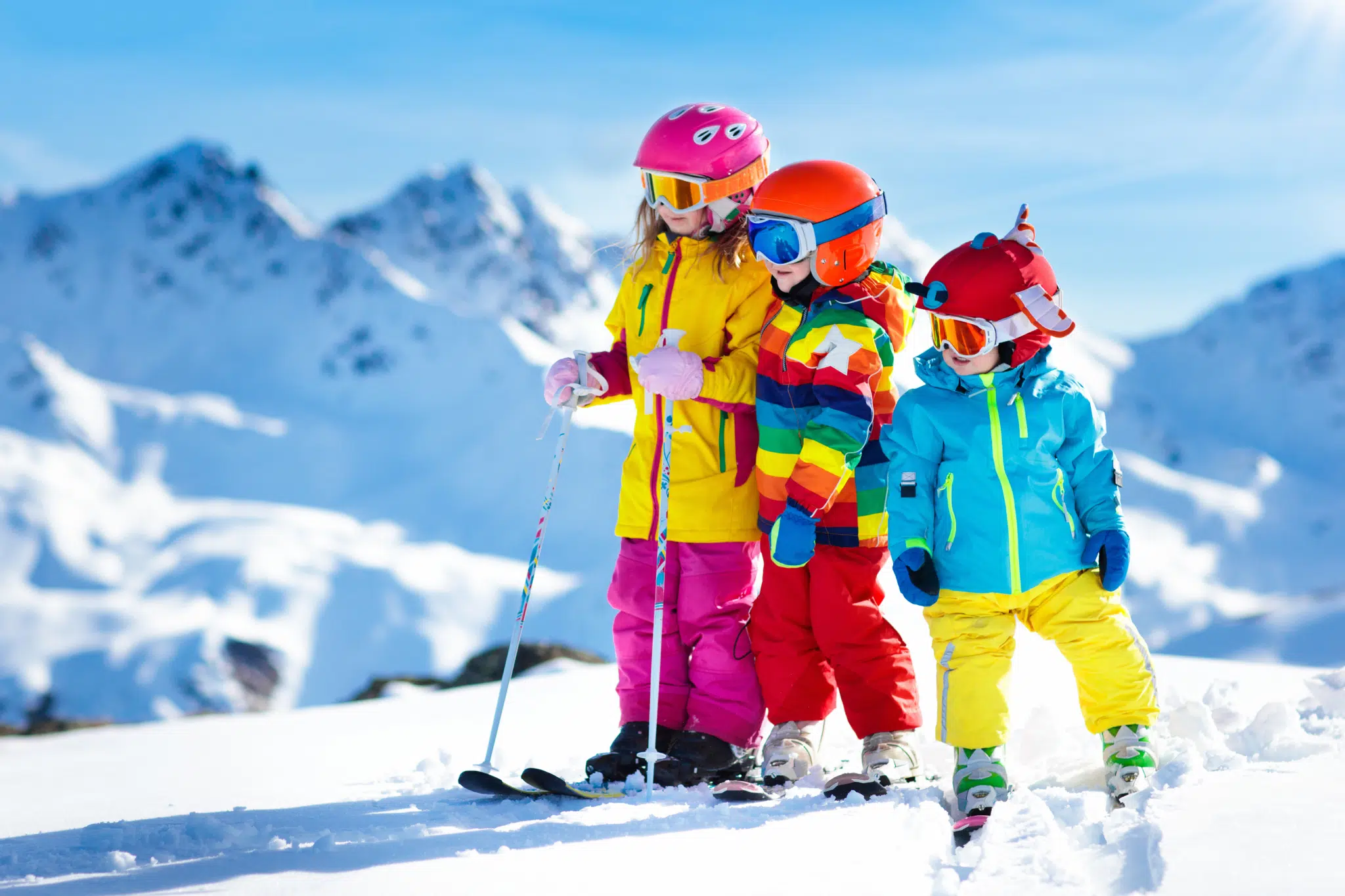 Ihr seht Kinder beim Skifahren auf der verschneiten Skipiste mit Bergen im Hintergrund.