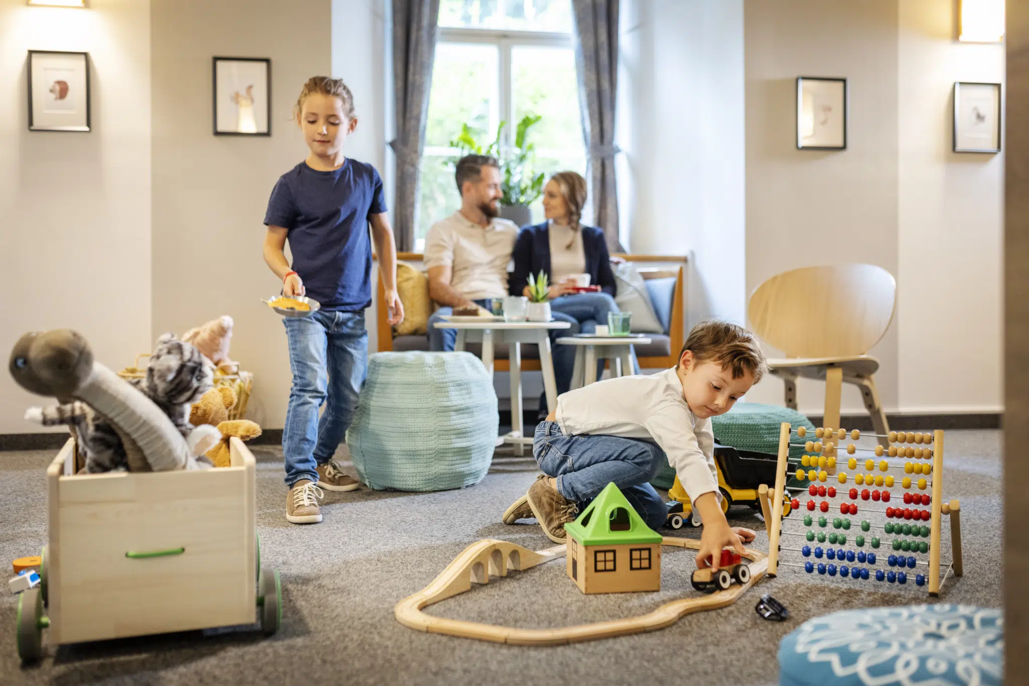 Ihr seht Kinder in der Spieleecke spielen, im Hintergrund sieht man die Eltern mit einem Kaffee an einem Tisch sitzen. JUFA Hotels bietet kinderfreundlichen und erlebnisreichen Urlaub für die ganze Familie.